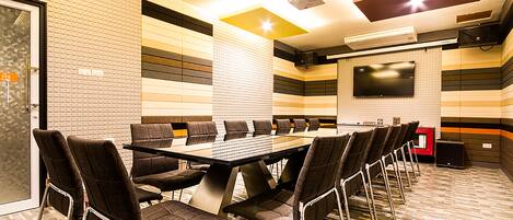 A conference room with a long table and chairs, a flat-screen TV, and a ceiling-mounted projector.