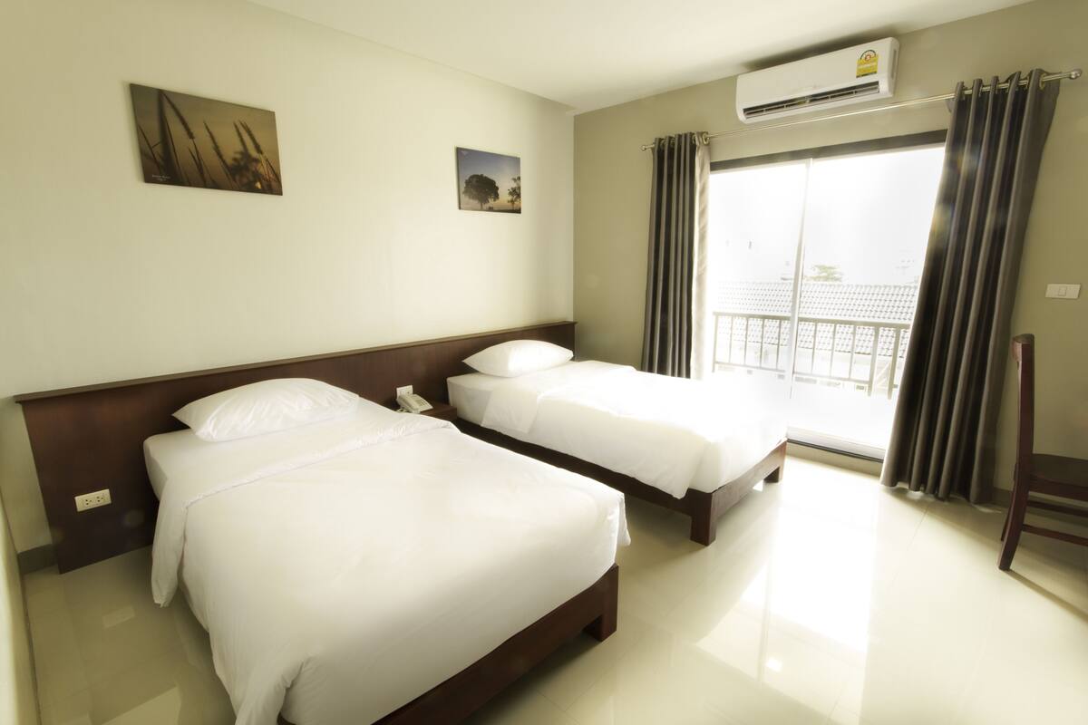 Een hotelkamer met twee bedden, een raam met gordijnen, een airconditioning en kunst aan de muur.