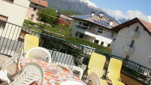 A terrace with outdoor seating, a mountain view, and a building with solar panels. - B&B Villa Norma (Feltre)