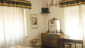 A bedroom with a bed, dresser, chairs, a mirror, and a chandelier. - B&B Villa Norma (Feltre)