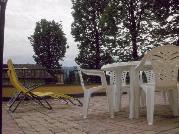 Outdoor patio furniture including chairs and a table, with a brick floor and trees in the background.
