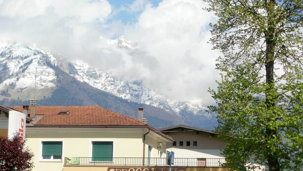 A building with a sign reading "PROGETTO" and a mountain with snow-capped peaks in the background. - B&B Villa Norma (Feltre)