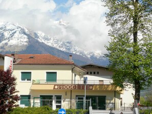 A building with a sign reading "PROGETTO" and a mountain with snow-capped peaks in the background.