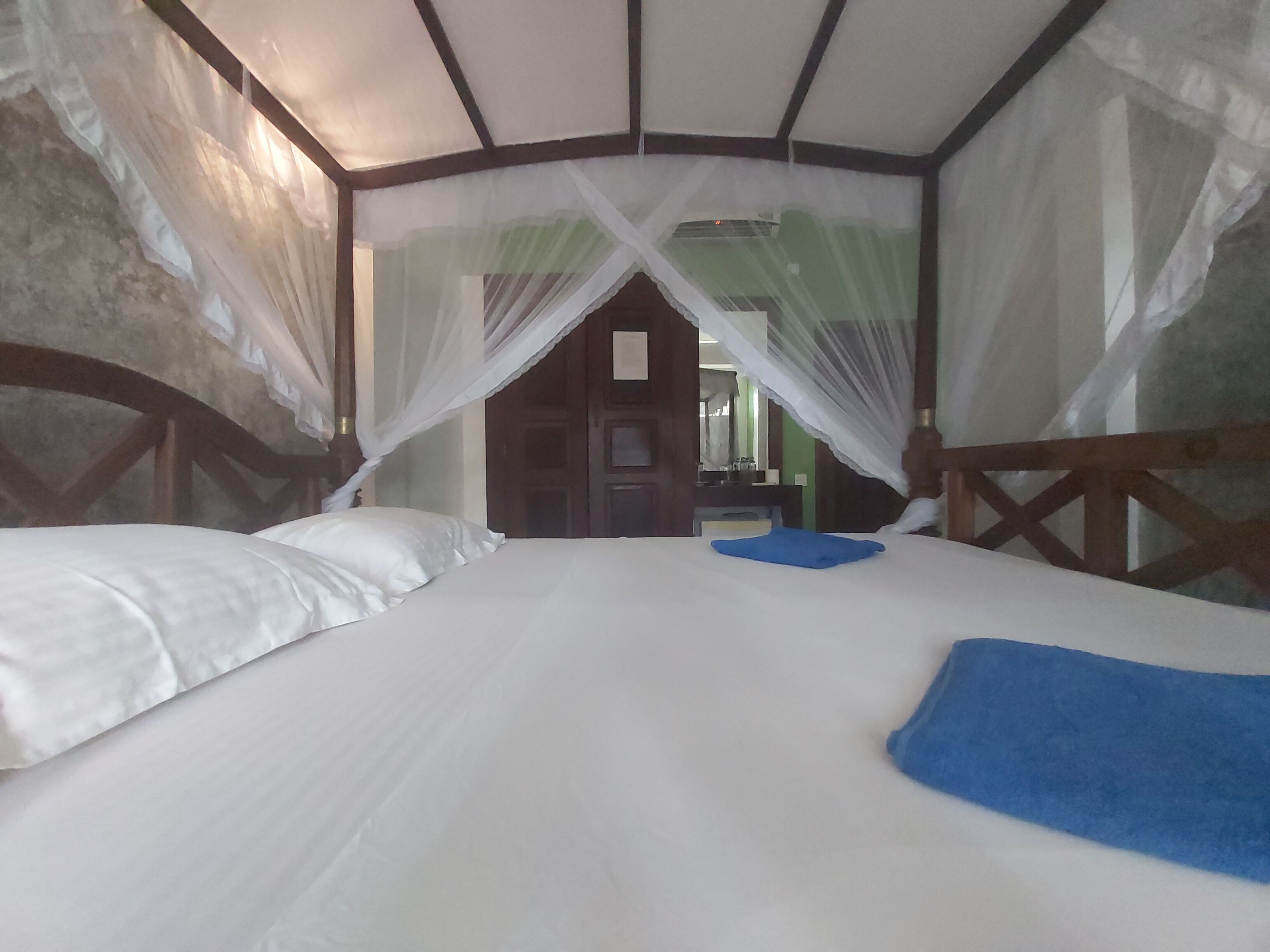 Una cama con sábanas blancas, una toalla azul y un dosel contra mosquitos.