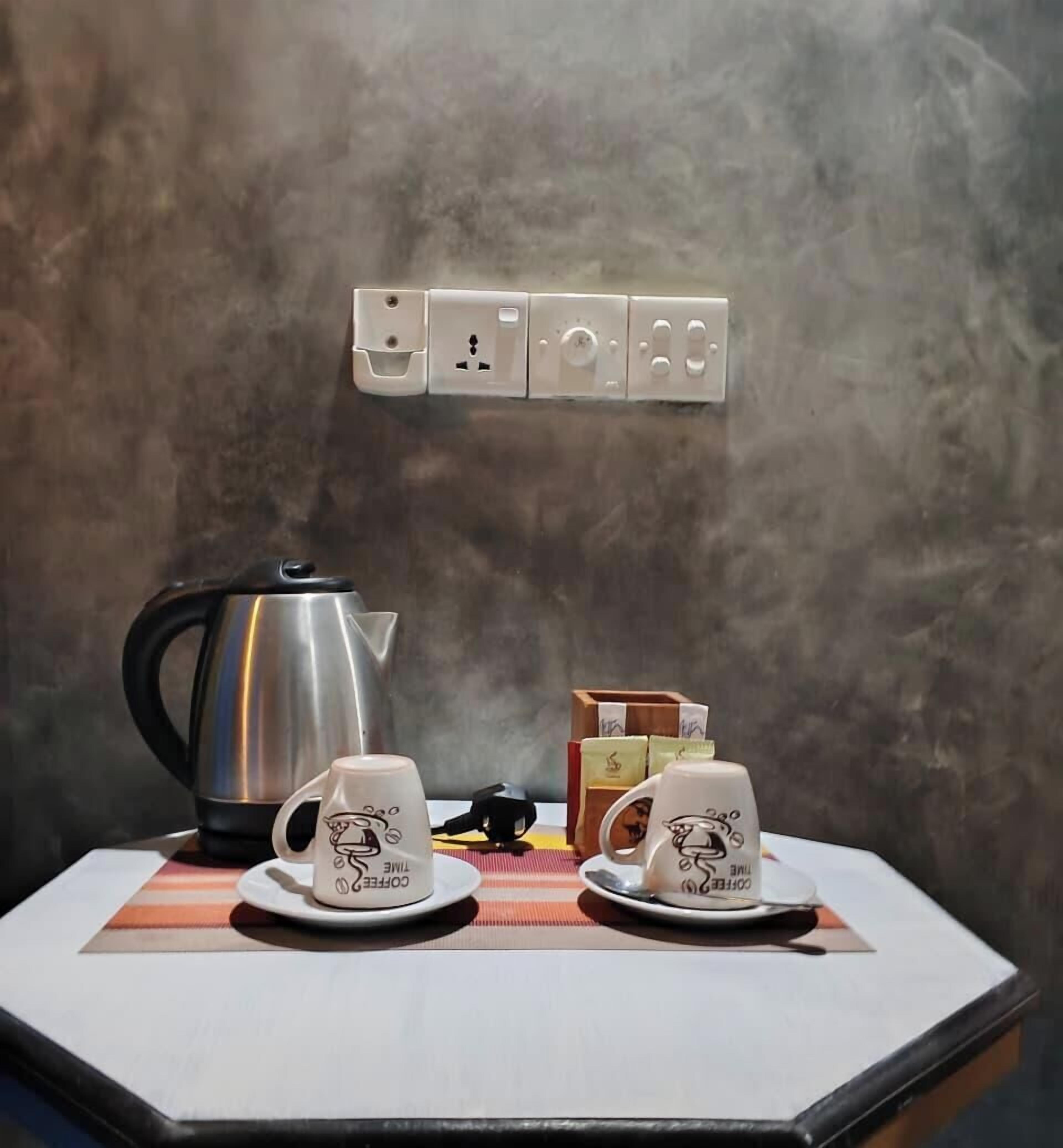 A table with a coffee maker, two cups, and a box of tissues.