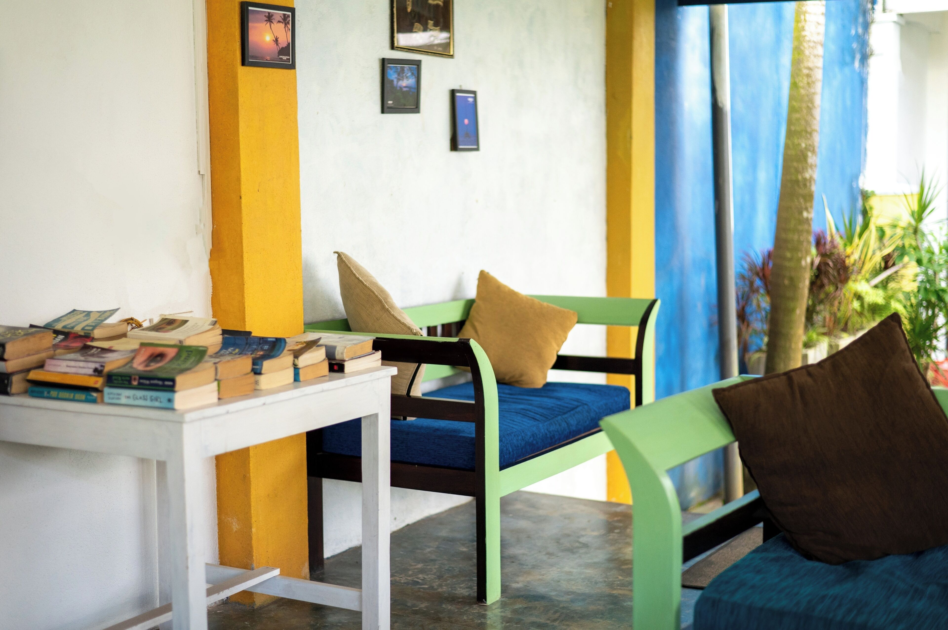 Une pièce avec un canapé vert et bleu, une table blanche sur laquelle sont posés des livres et un mur jaune orné de tableaux.