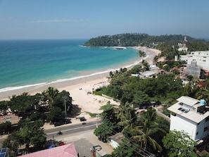 A coastal town with a beach, buildings, and a hill with dense vegetation. - Aaradhya Mirissa (Mirissa)