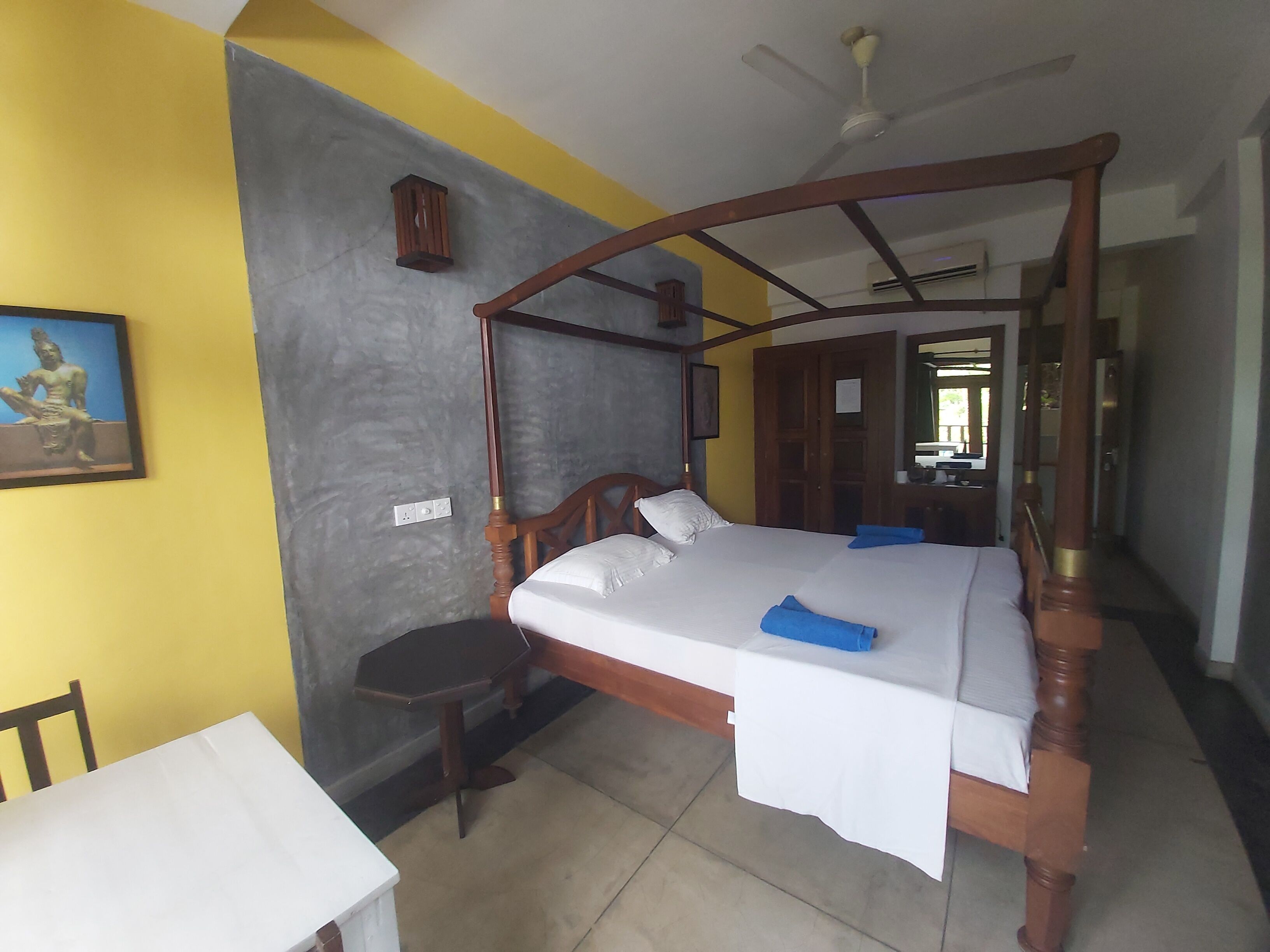 Una habitación con una cama con dosel, una mesita, una silla y una estatua en la pared.