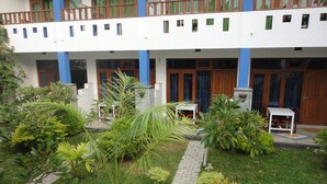 A building with a white facade, blue pillars, and a balcony with wooden railings. There is a paved pathway leading to a small seating area with a table and chairs. - Aaradhya Mirissa (Mirissa)