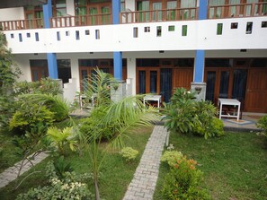 A building with a white facade, blue pillars, and a balcony with wooden railings. There is a paved pathway leading to a small seating area with a table and chairs. - Aaradhya Mirissa (Mirissa)