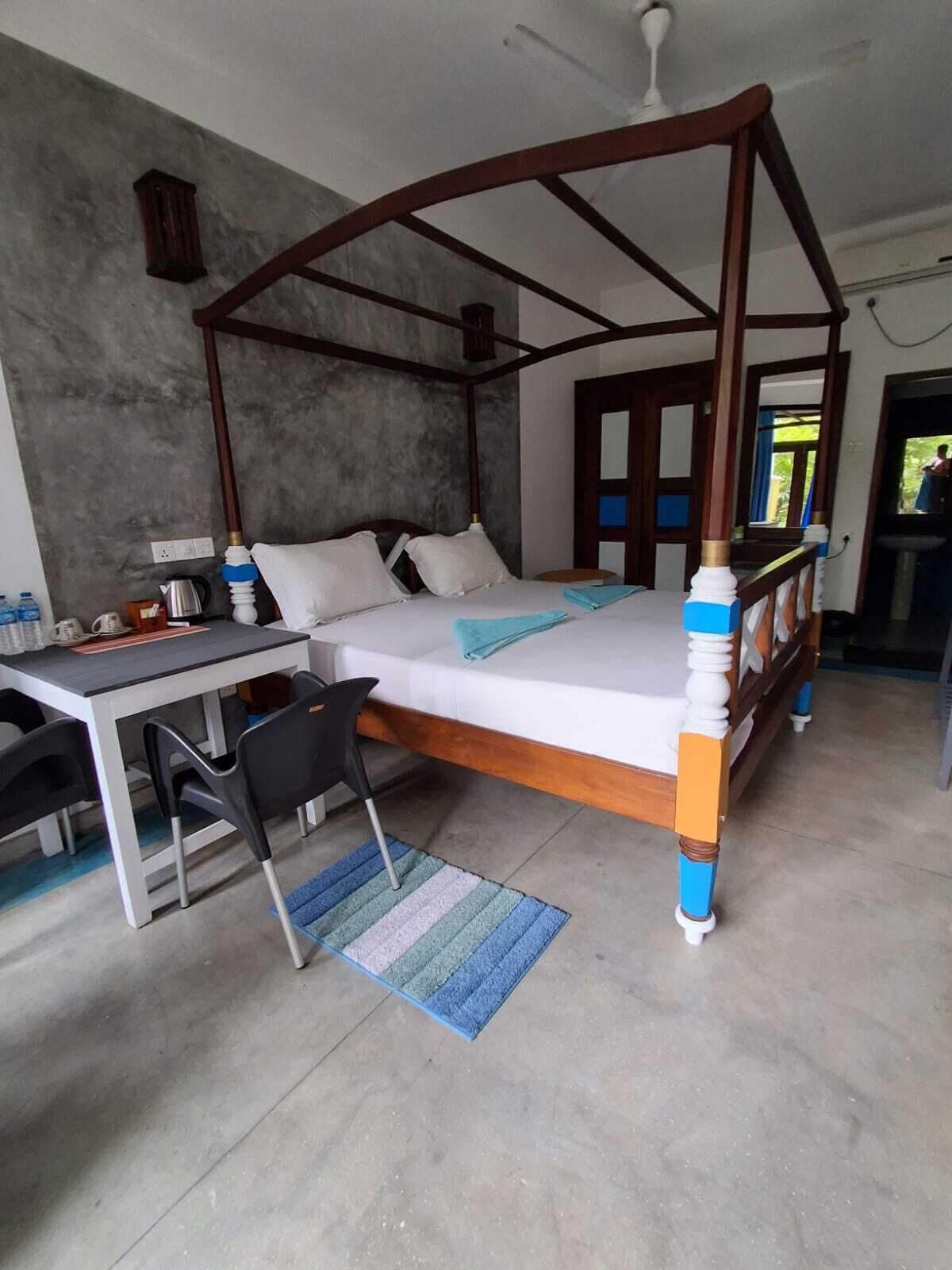 A four-poster bed with a desk and chairs, a small rug, and a view of the outdoors.