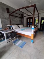 A four-poster bed with a desk and chairs, a small rug, and a view of the outdoors.