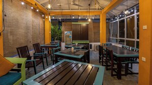 A restaurant with wooden tables and chairs, a ceiling fan, and large windows. - Aaradhya Mirissa (Mirissa)