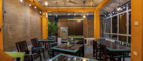Un restaurant avec des tables et des chaises en bois, un ventilateur de plafond et de grandes fenêtres.