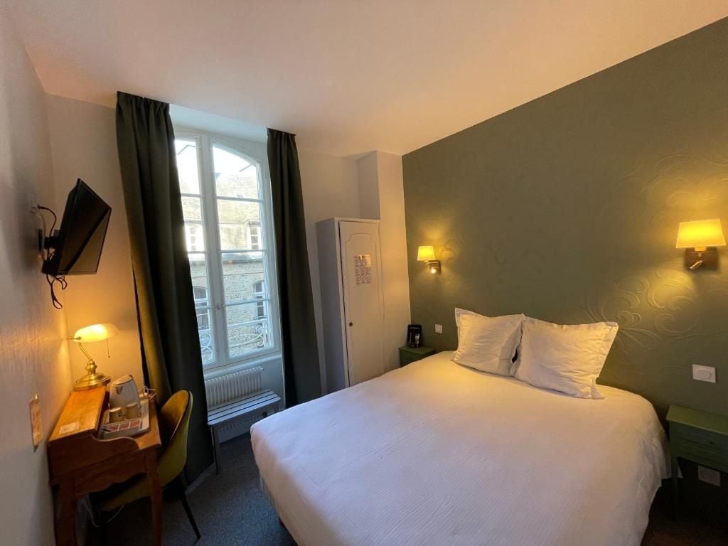 A hotel room with a bed, a desk with a chair, a television, and a window with curtains.