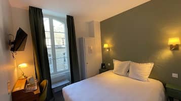 A hotel room with a bed, a desk with a chair, a television, and a window with curtains.