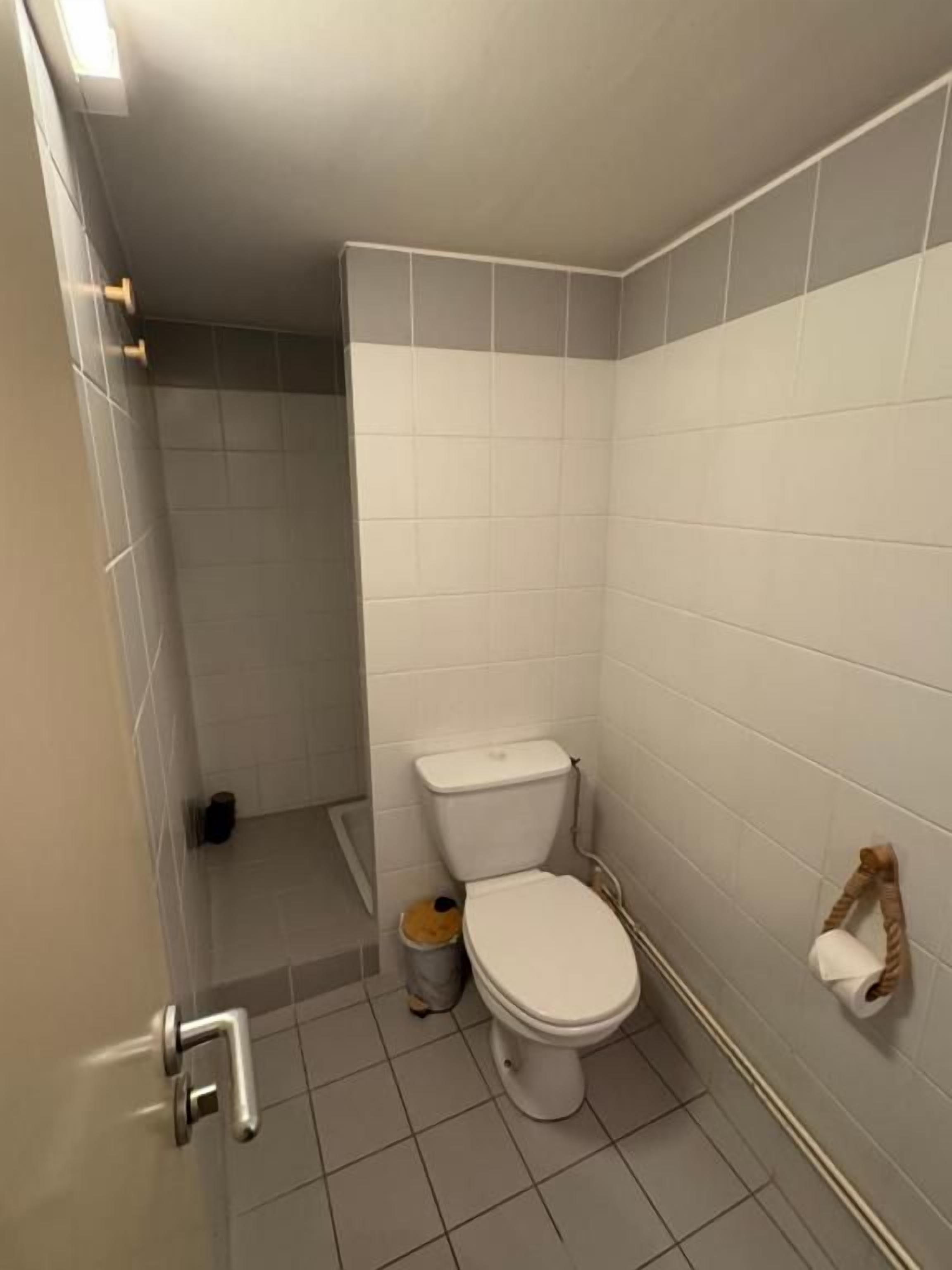 Ein kleines Badezimmer mit Fliesen, einer Toilette, einem Mülleimer und einem Handtuchhalter.