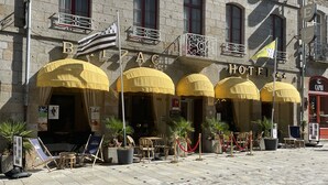 A hotel facade with multiple yellow awnings, outdoor seating, and a stone building. - Balzac Hôtel (Fougeres)