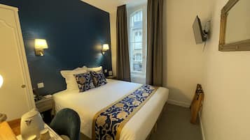 Habitación de hotel con una cama grande, un escritorio con hervidor y tazas, una silla y vistas a un edificio a través de la ventana.