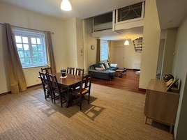 Amplia sala de estar con mesa y sillas de comedor, un sofá y una escalera que sube a un nivel superior.