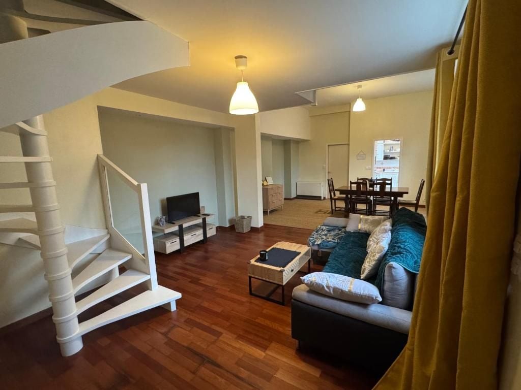 Een moderne woonkamer met een trap, een bank, een salontafel en een eethoek op de achtergrond.