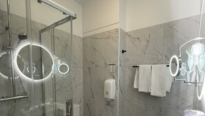 A modern bathroom with a glass-enclosed shower, a toilet, a sink with a mirror, and a marble-tiled wall. - Balzac Hôtel (Fougeres)