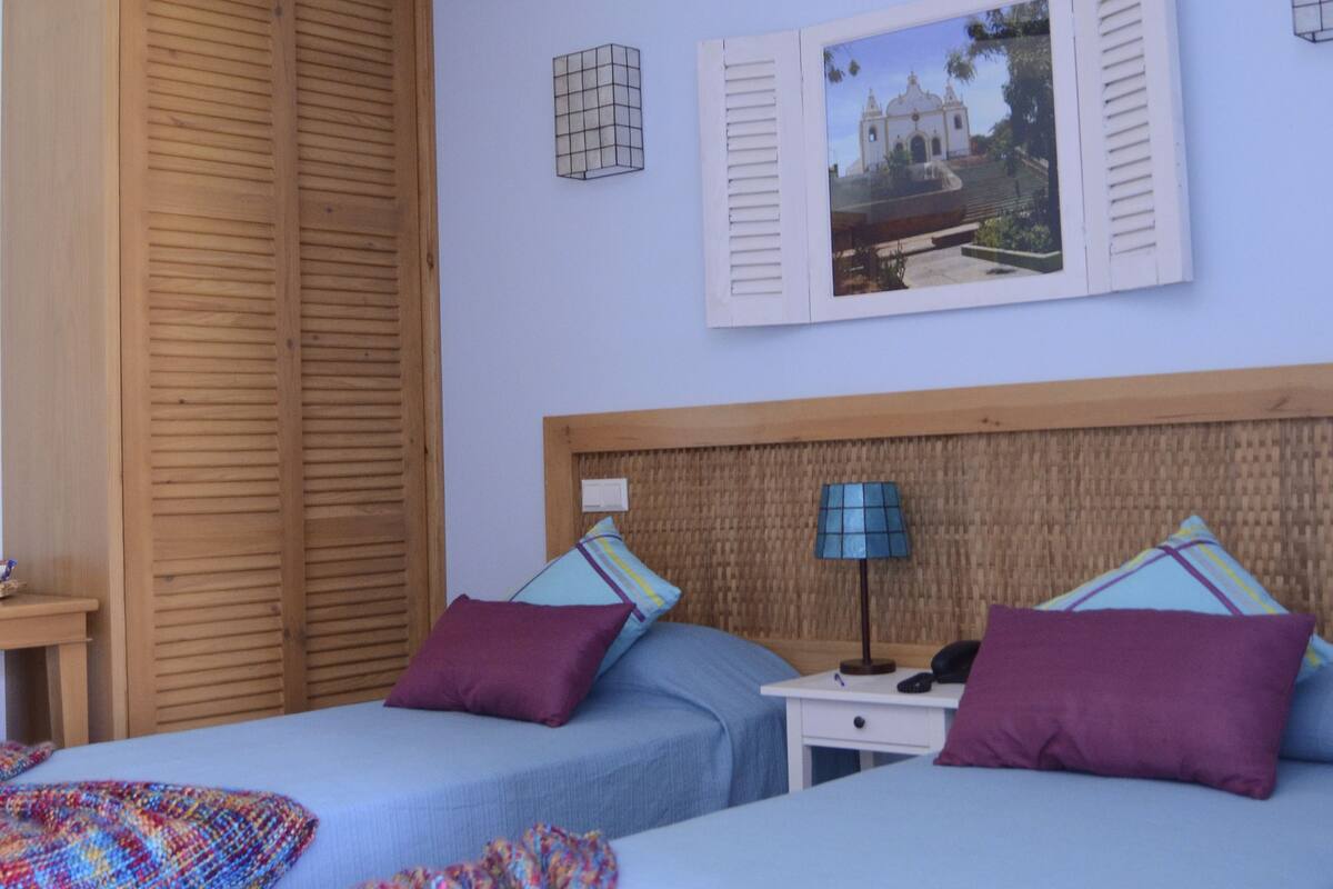 A bedroom with two beds, a ceiling fan, wooden wardrobe, and a wall-mounted picture.