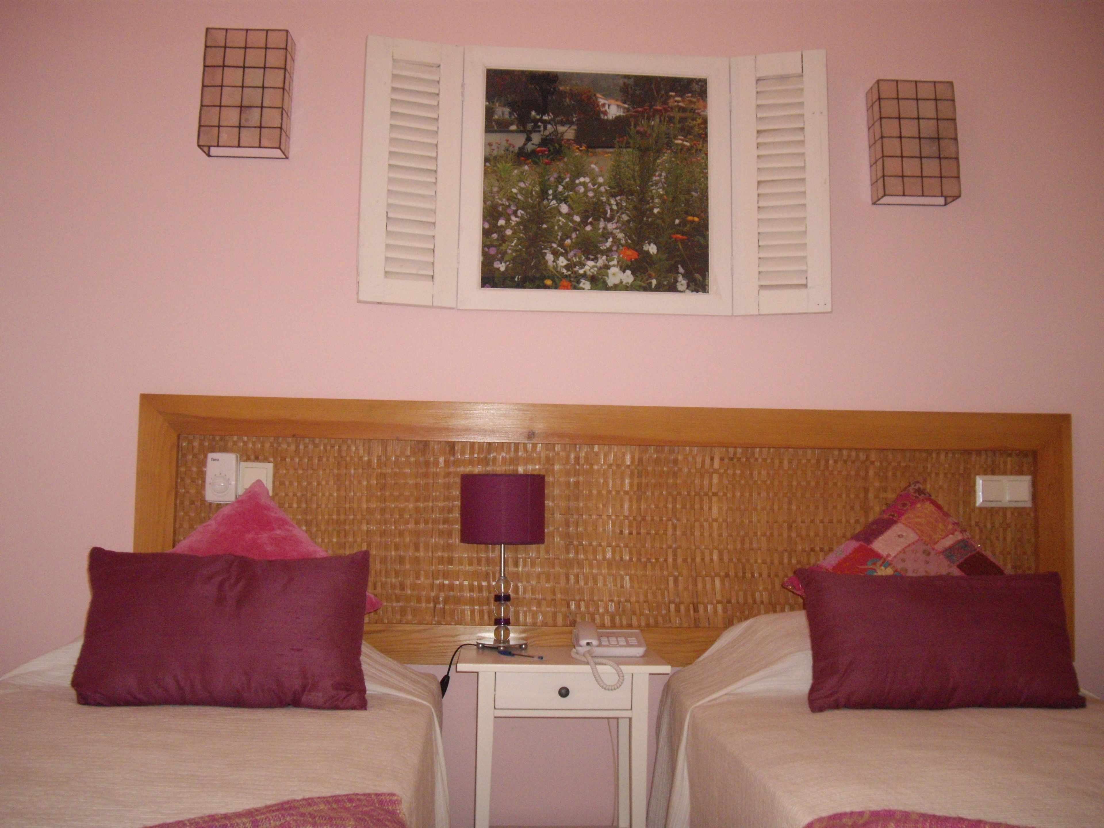 A hotel room with two beds, a nightstand, a lamp, and a painting on the wall.