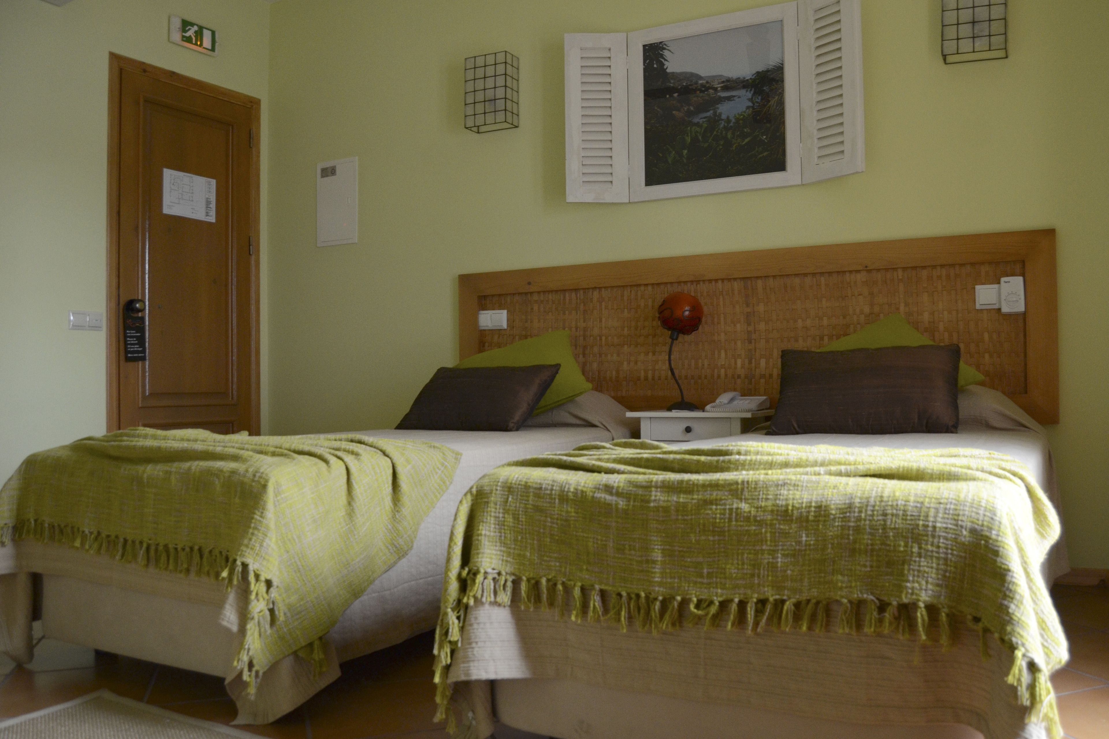 A room with two beds, a wooden headboard, a nightstand, and a wall-mounted picture.