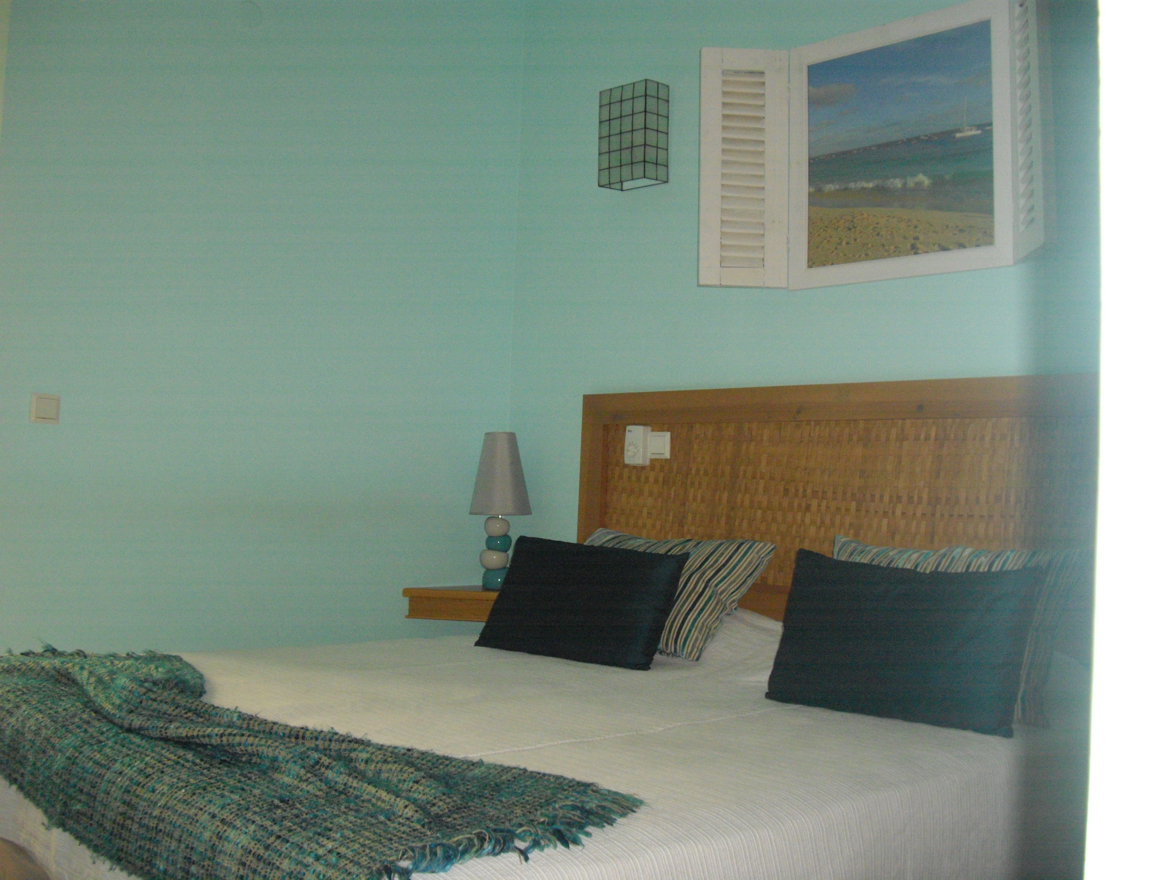 Ein Schlafzimmer mit Bett, Kissen, einer Lampe, einem Bild an der Wand und einer Decke.