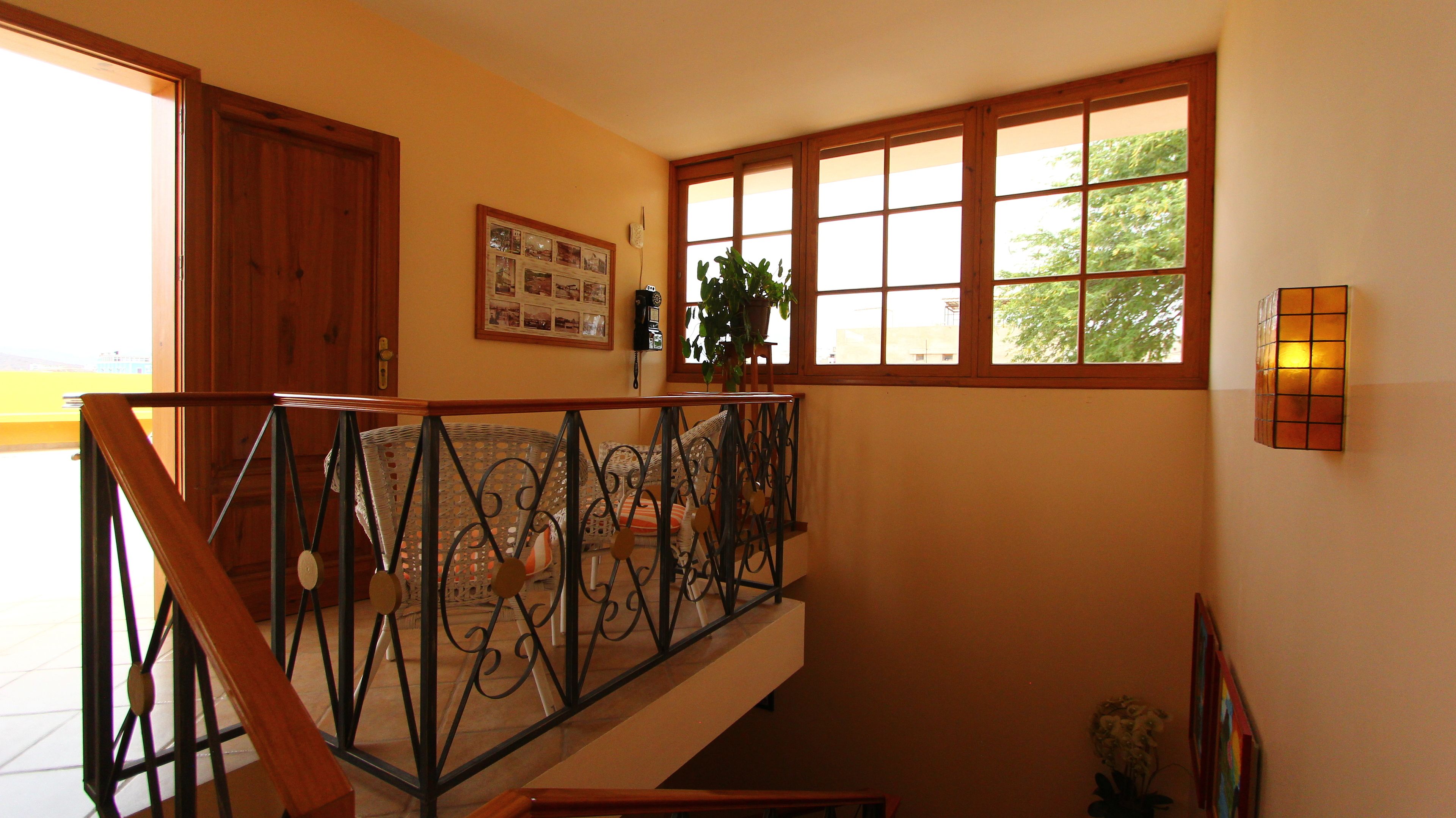 A staircase with a wrought iron railing, a wooden door, a framed collage on the wall, and a window with a view of trees.