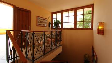 A staircase with a wrought iron railing, a wooden door, a framed collage on the wall, and a window with a view of trees.