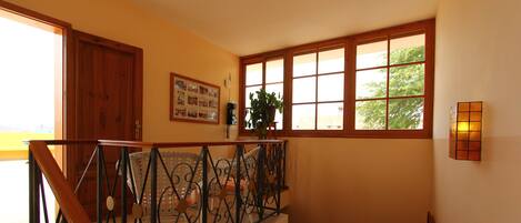A staircase with a wrought iron railing, a wooden door, a framed collage on the wall, and a window with a view of trees.