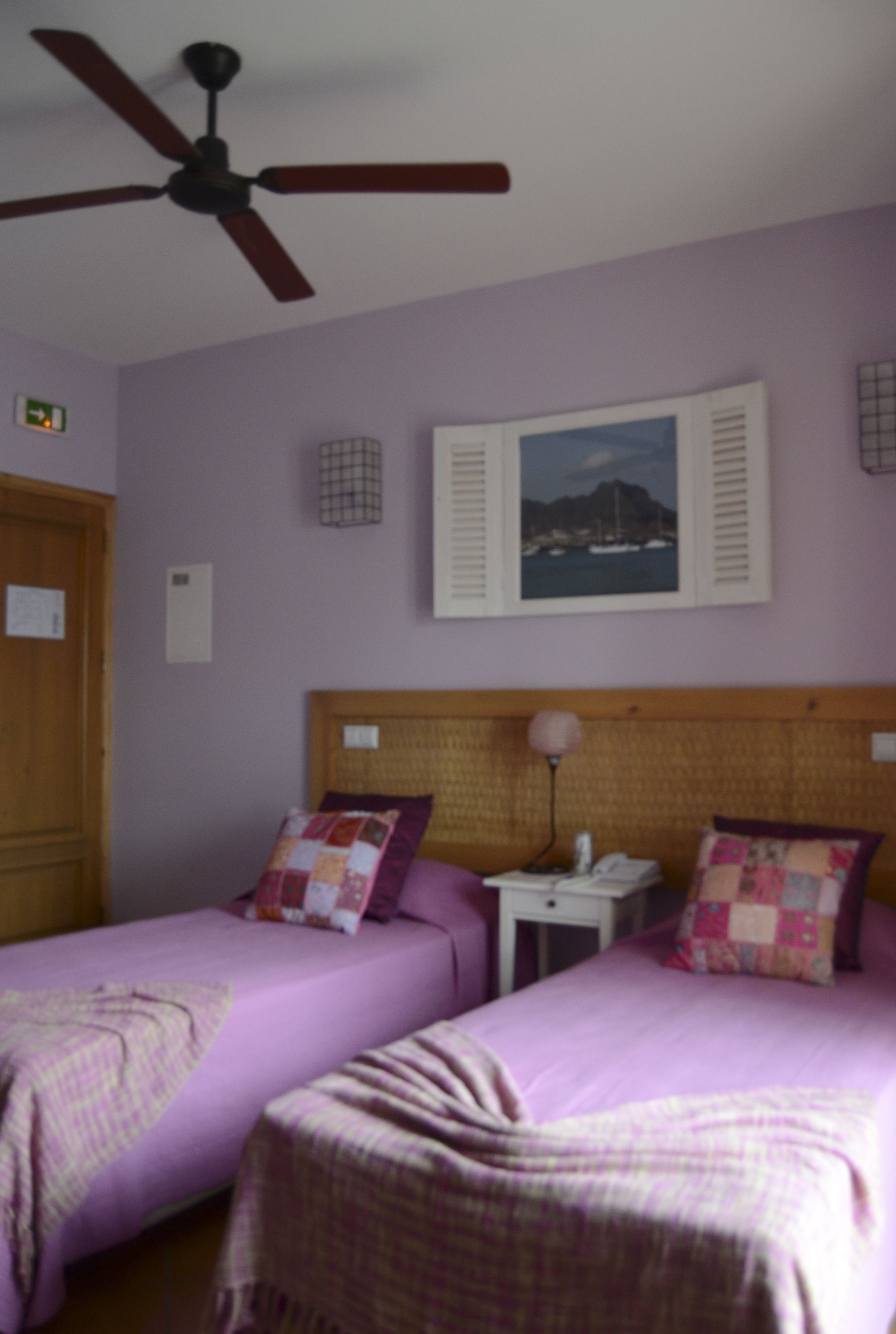 Ein Schlafzimmer mit zwei Betten, einem Deckenventilator, einem Nachttisch und einem an der Wand hängenden Bild.