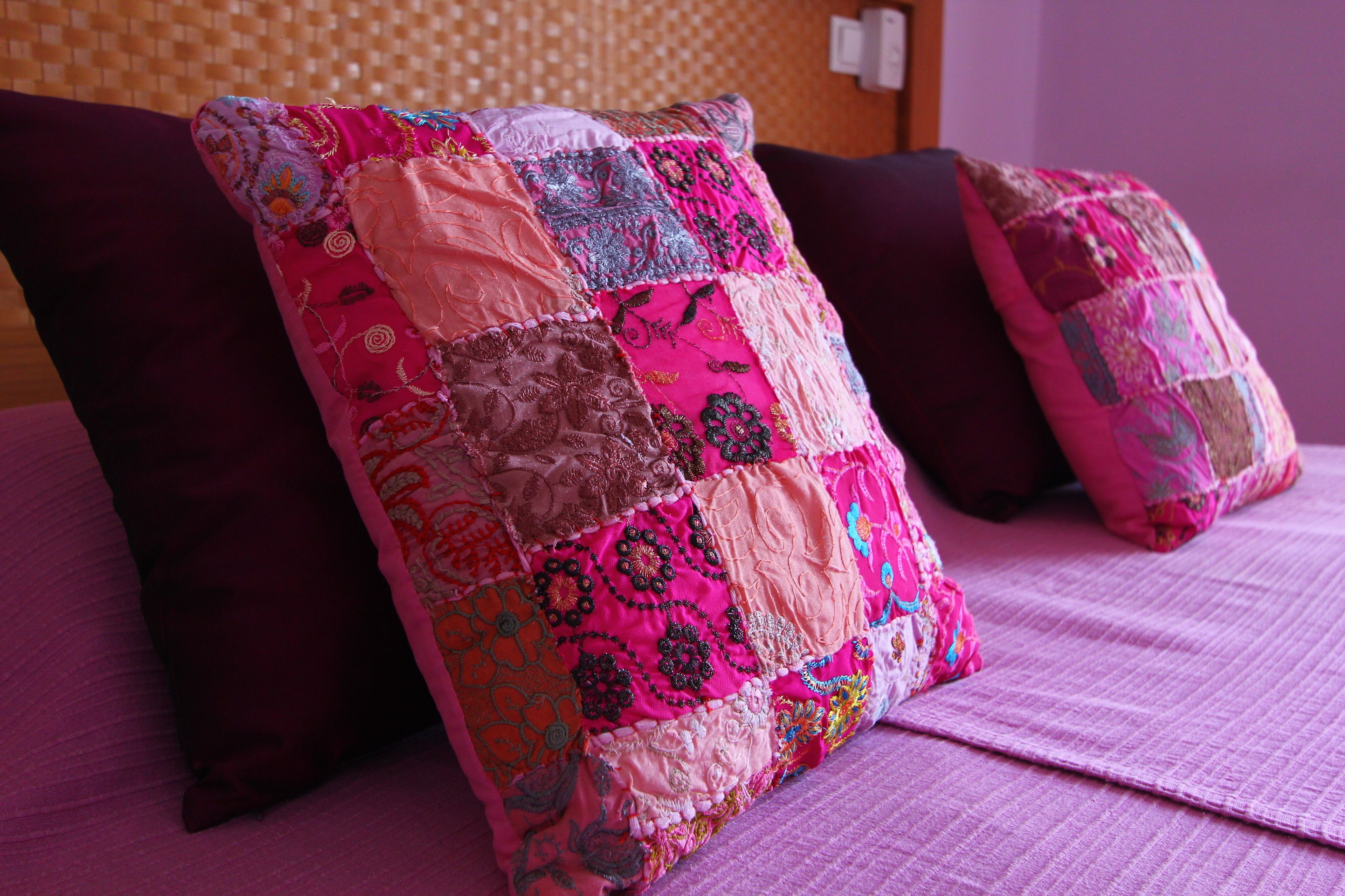 Una cama con un edredón rosa y dos almohadas oscuras.