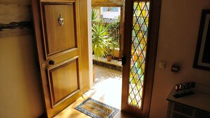 Una puerta de madera con un picaporte metálico, una puerta de cristal con un diseño de cuadrícula y un piso de baldosas.