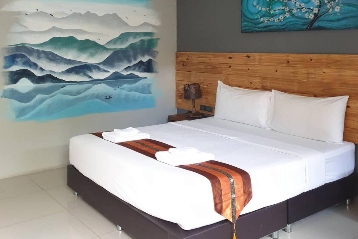 Ein modernes Schlafzimmer mit einem großen Bett, einem hölzernen Kopfteil, einem Gemälde von Bergen und einem Gemälde eines Baumes.