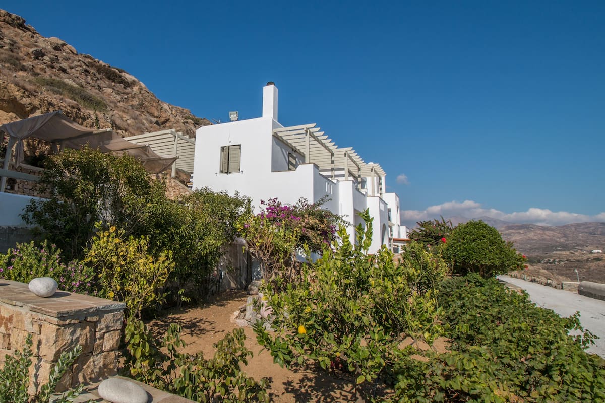 A white building with a stone pathway leading to it, surrounded by greenery and a clear blue sky.