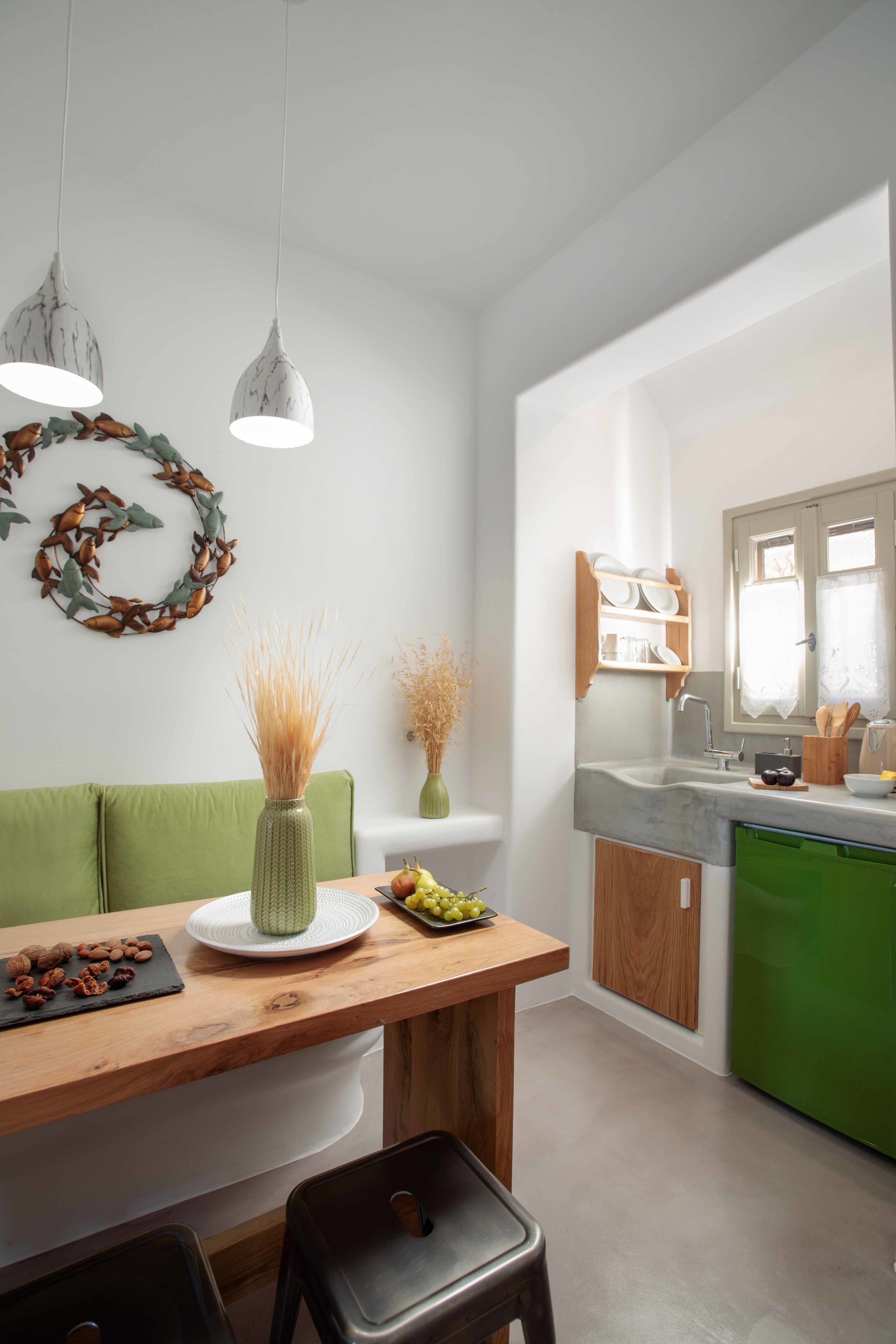 Cocina moderna con una mesa de madera, dos lámparas colgantes, un sofá verde y un lavavajillas verde.