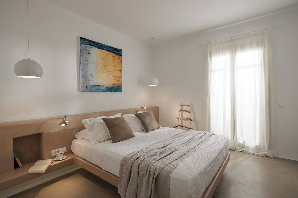 A bedroom with a bed, bedside table, reading lamp, and a painting on the wall.