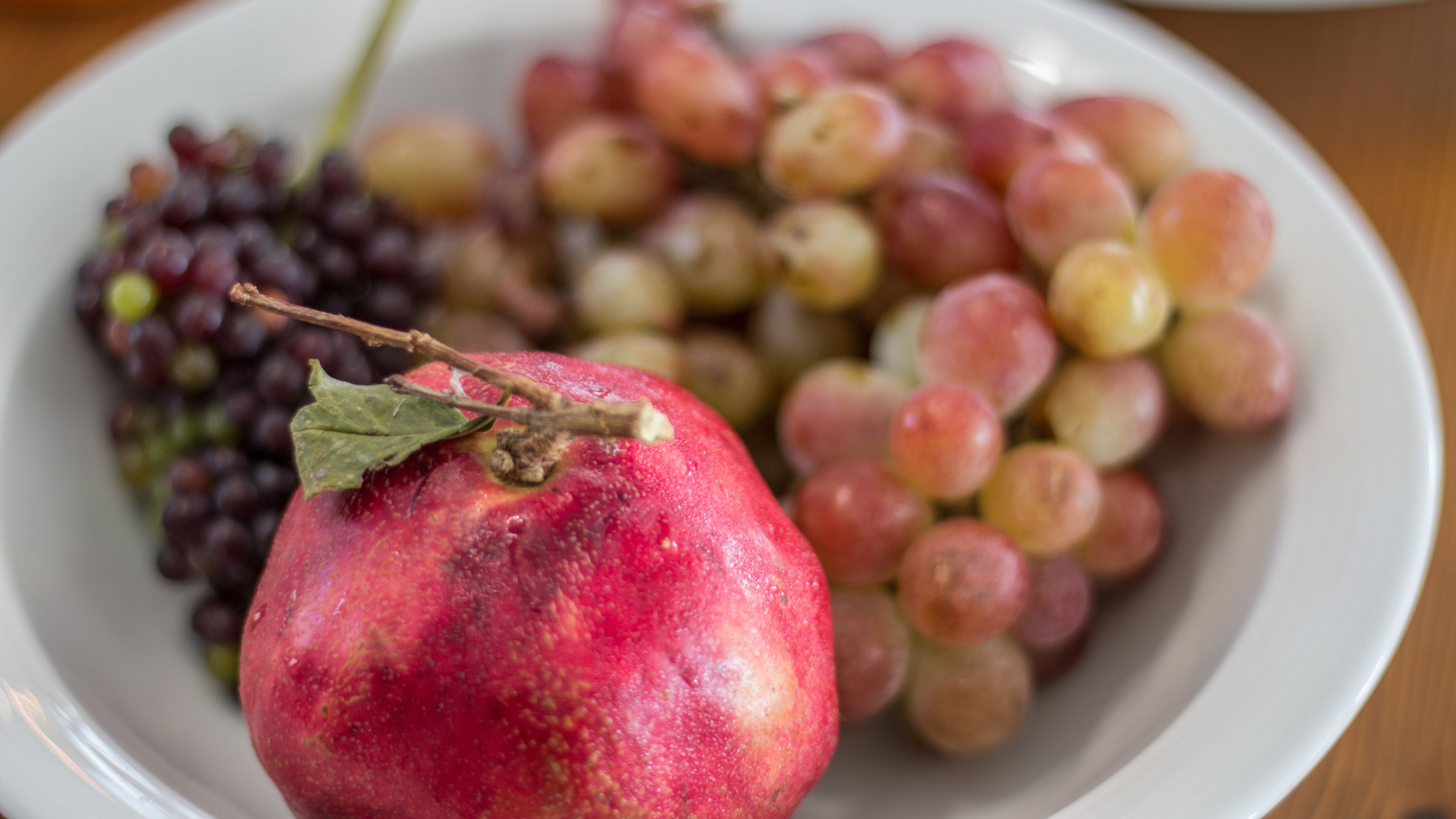 A plate with a red fruit, possibly a pomegranate, and a bunch of grapes.