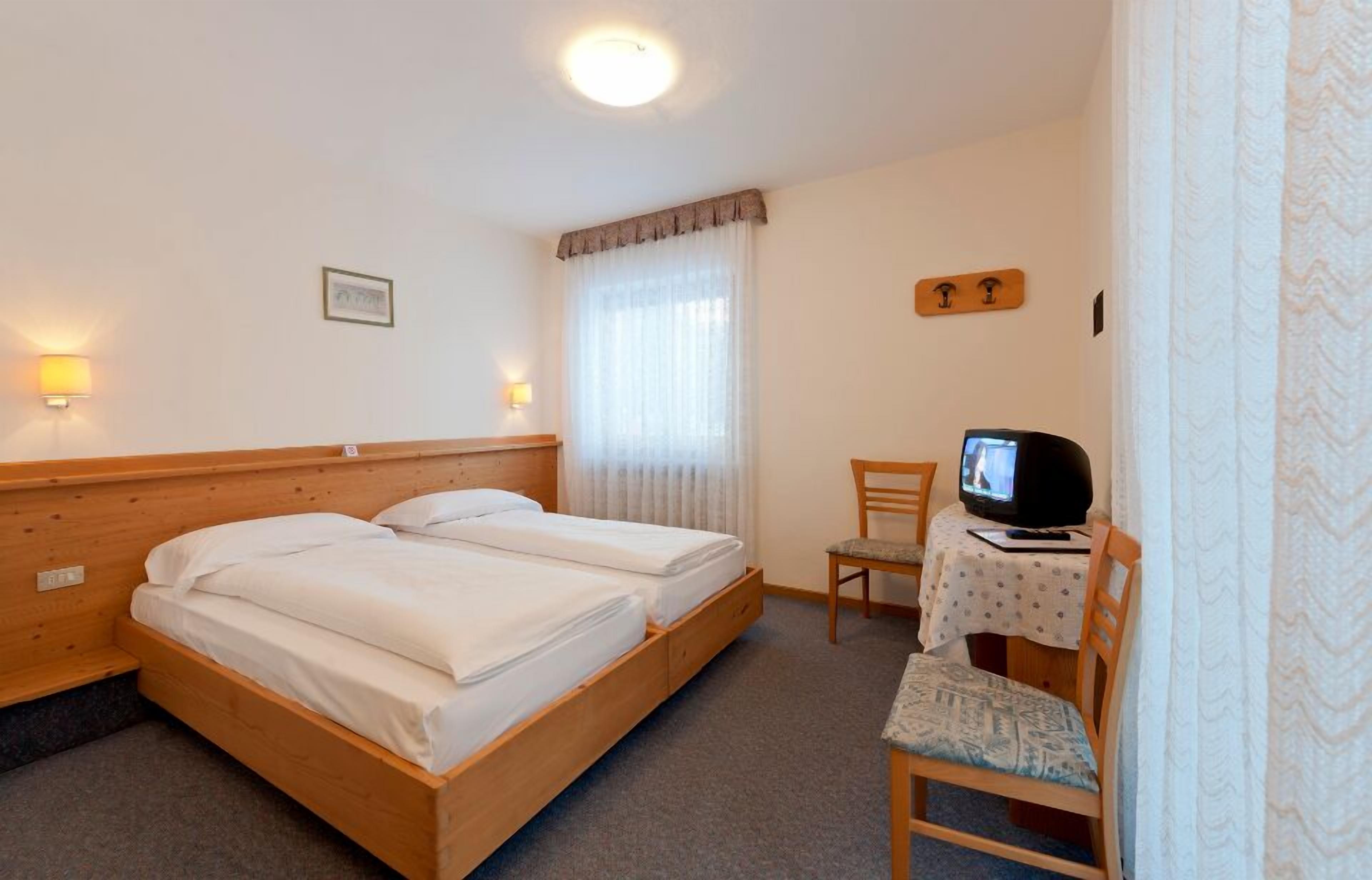 A bedroom with a wooden bed, a television on a small table, and a chair.