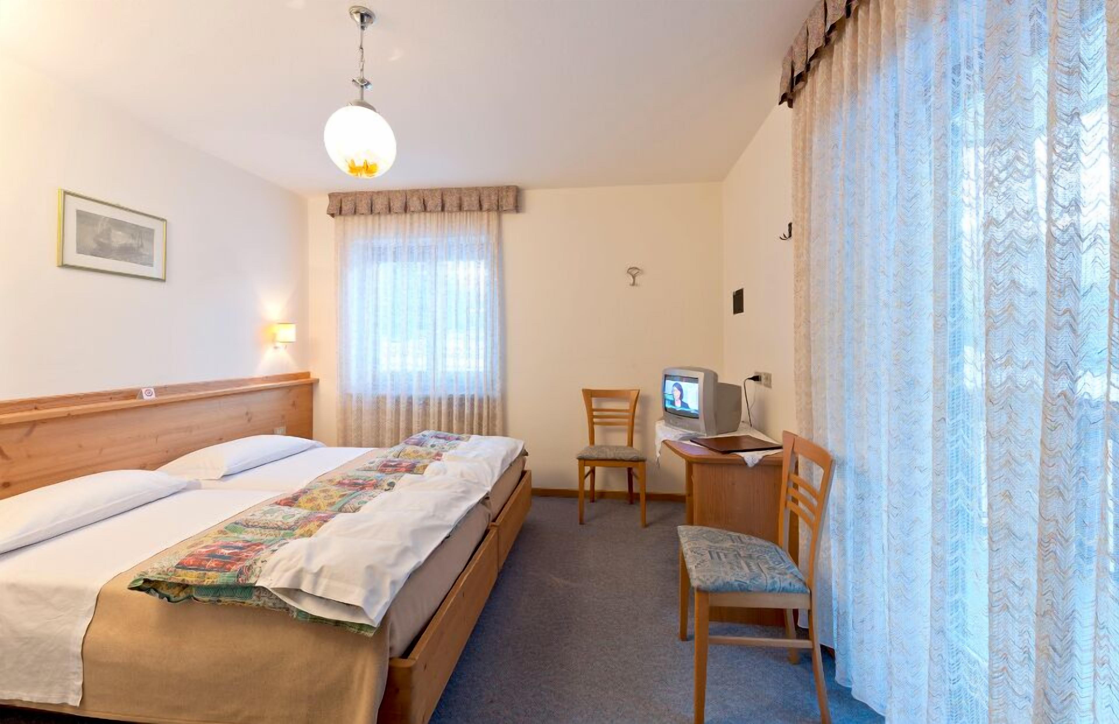 Ein Hotelzimmer mit einem hölzernen Bett, einem Schreibtisch mit Computer, einem Sessel und einem Fernseher.