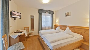 Ett hotellrum med en säng i trä, ett skrivbord med en stol, en spegel och en tv på väggen.
