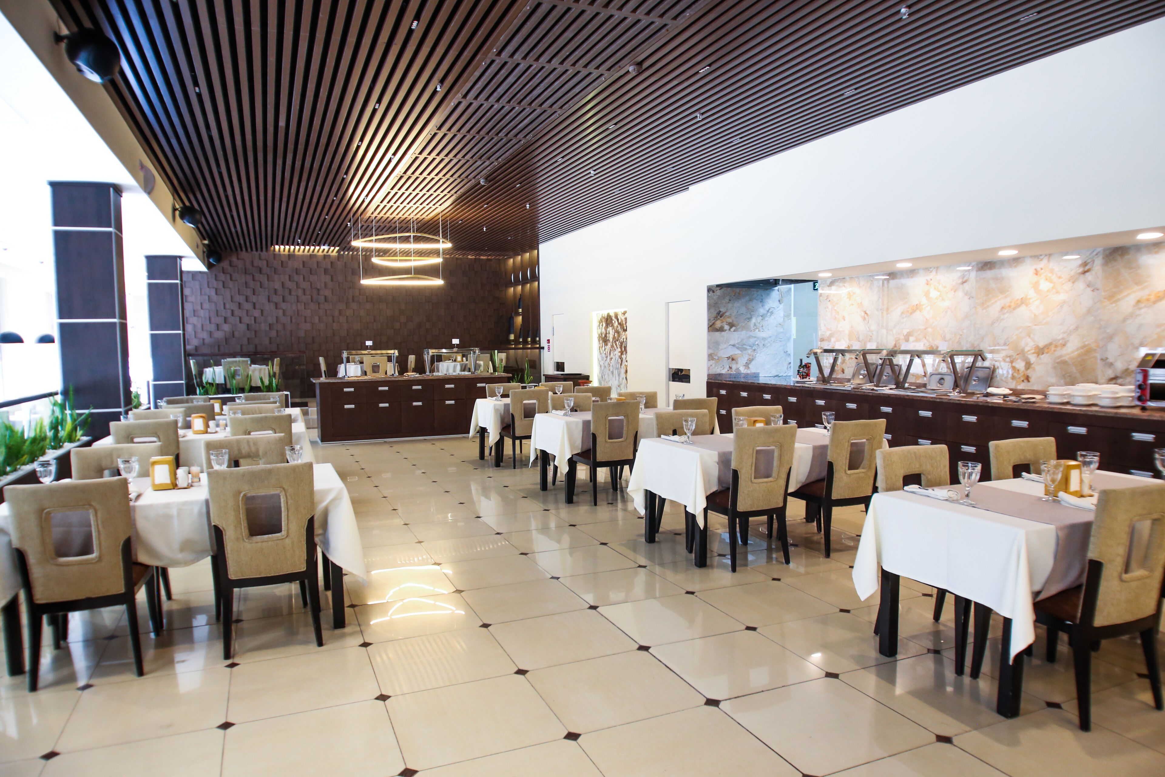 A spacious dining area with multiple tables and chairs, a polished tiled floor, and a modern ceiling design.