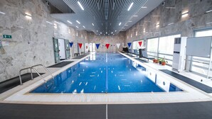 An indoor swimming pool with clear lane markings, a diving board, and a ceiling with linear lighting fixtures. - Chagala Residence Atyrau (Atyrau)
