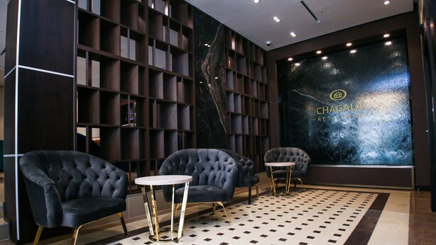 A modern lobby with dark wood shelving, three plush armchairs, and a patterned floor. - Chagala Residence Atyrau (Atyrau)