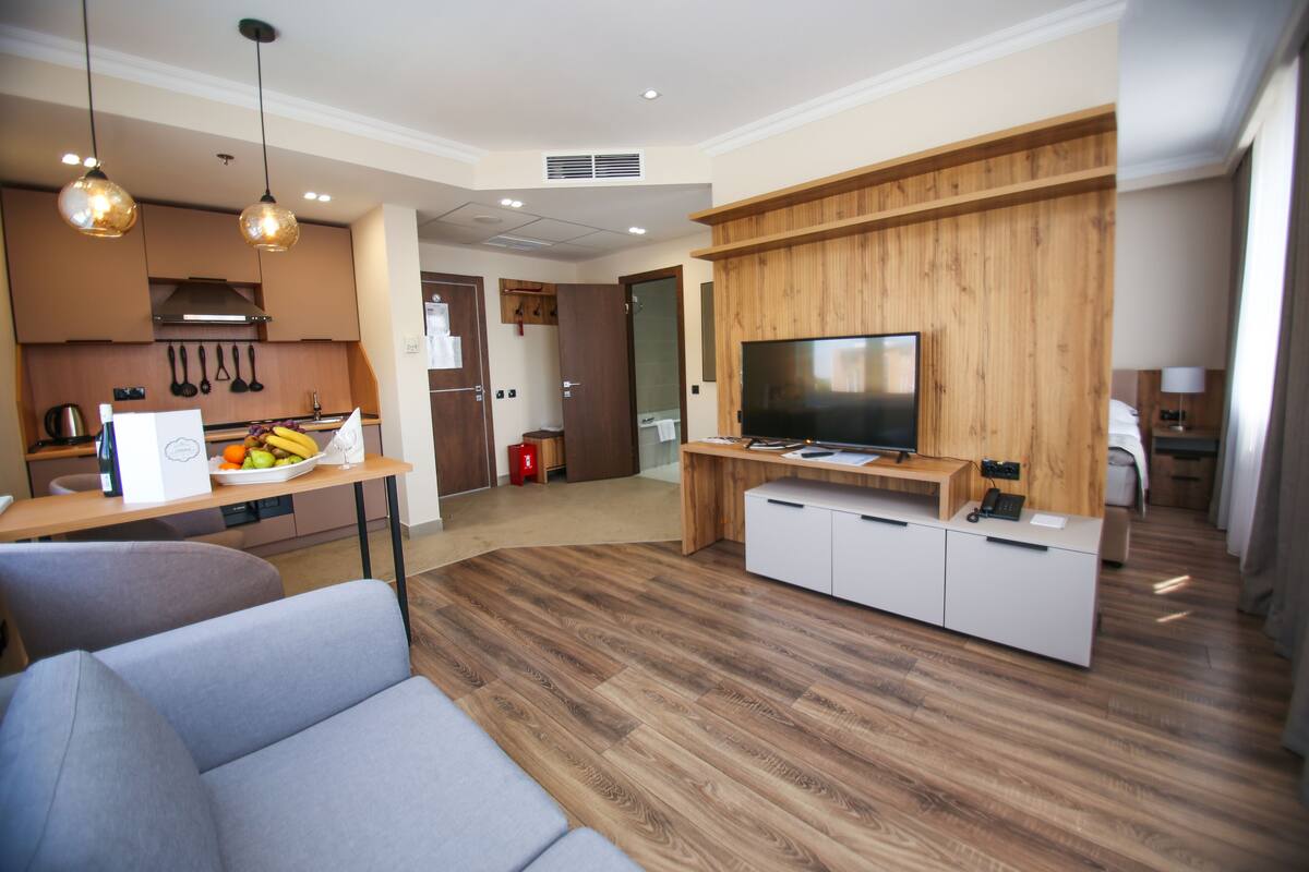 A modern living room with a sofa, a dining table with fruit, a TV, and wooden paneling.