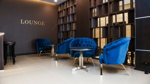 A lounge area with a 'LOUNGE' sign, blue upholstered chairs, a round table, and a bookshelf. - Chagala Residence Atyrau (Atyrau)