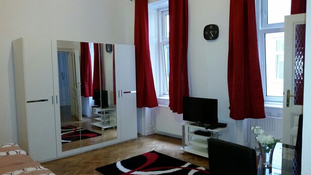 A room with a large mirror, a television, and a window with red curtains. - Goldfisch Apartment Central Park (Vienna)
